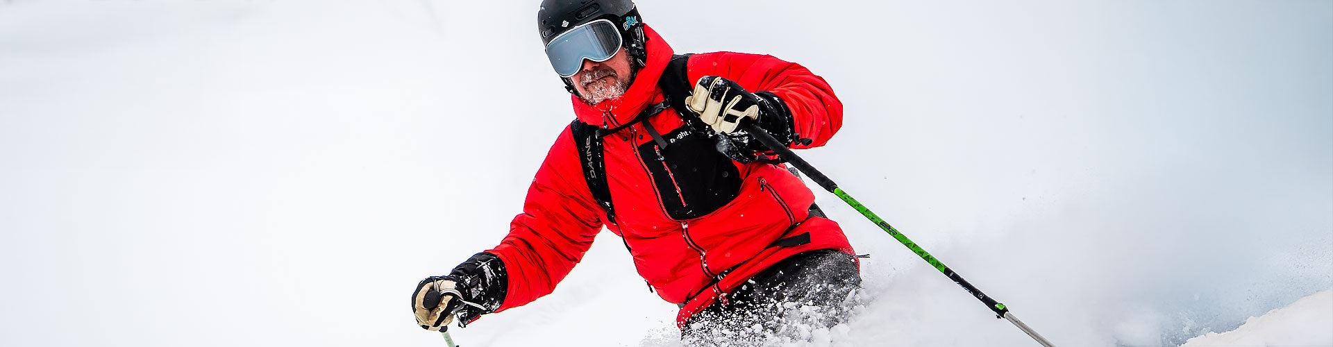 En man som åker skidor i lössnö, iklädd en klarröd Primaloft Hyperlight Jacket från Bright Equipment®