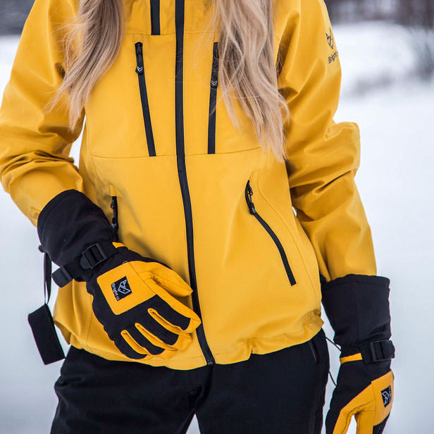 Blond kvinna med gul jacka, svarta byxor och gulsvarta handskar från Bright Equipment.