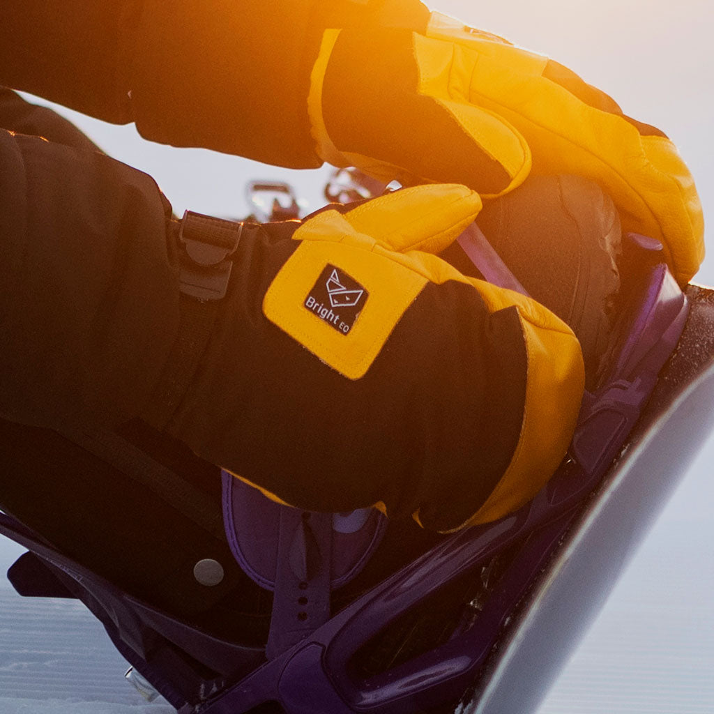 Gulsvarta handskar på snowboard-åkare i skidbacken.